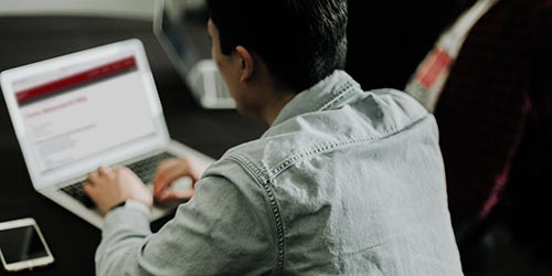 A young man looking at a FIH's webpage on a laptop.